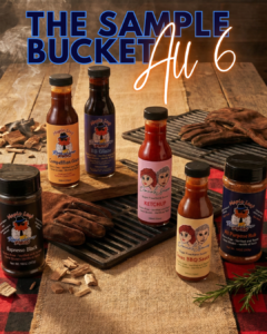 A collection of six BBQ sauces and rubs called The Sample Bucket, featuring Maple Leaf Roadhouse BBQ glazes and Donna’s Sauces Ketchup, arranged on a rustic wooden table with grill grates and wood chips.